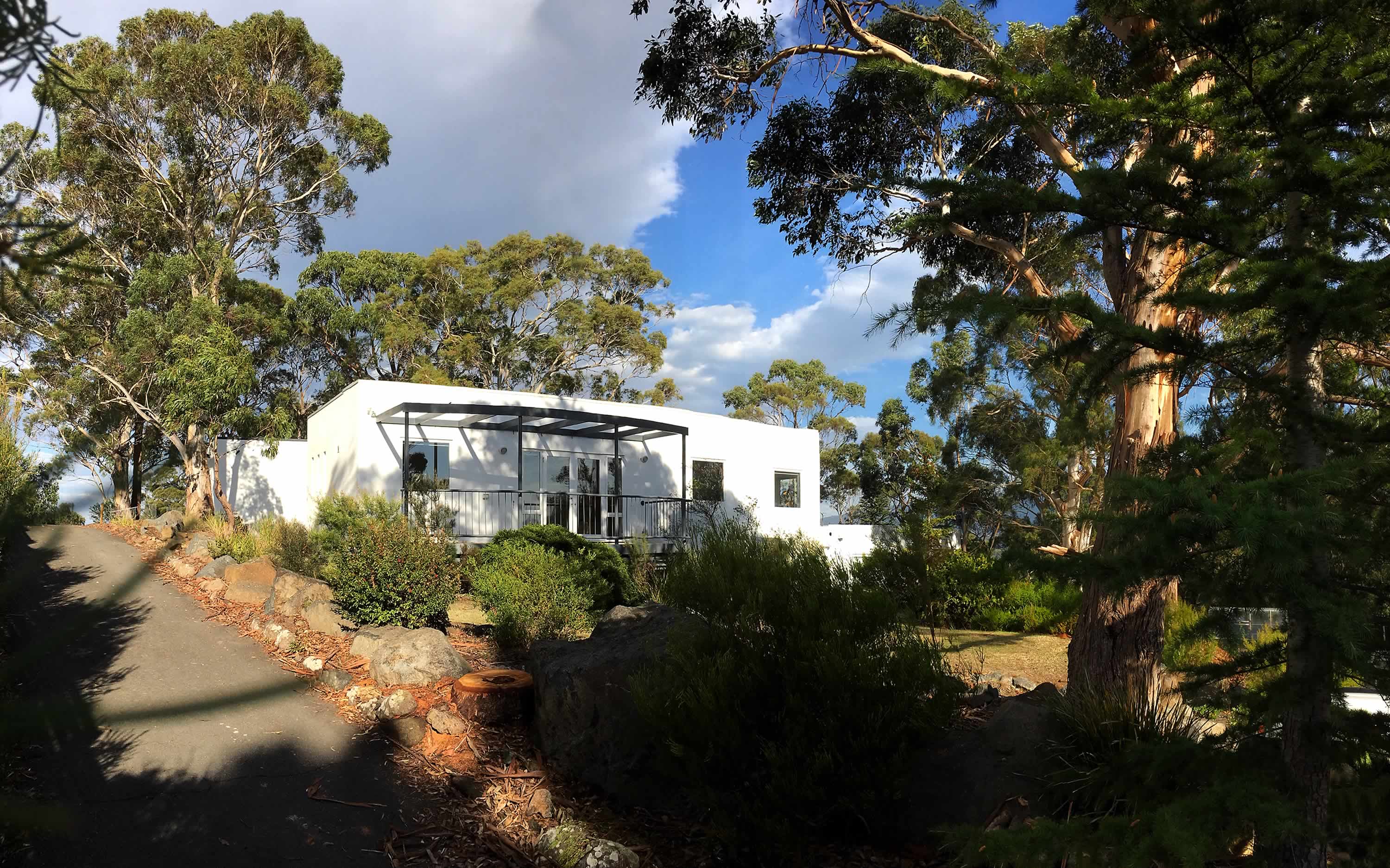 Photo of the OUTSIDE THE BOX exterior, a sunlit white modern building surrounded by eucalypts.