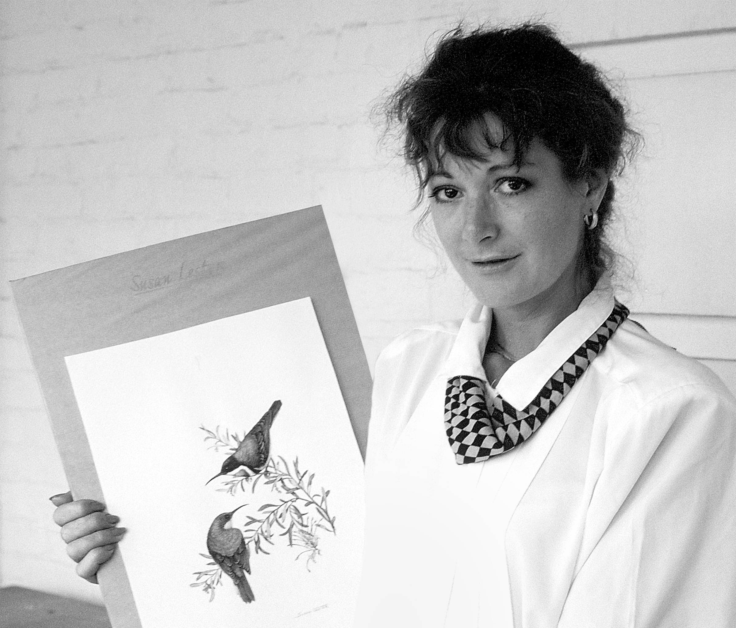 A black and white portrait of Susan Lester holding her watercolour of the Eastern Spinebill.