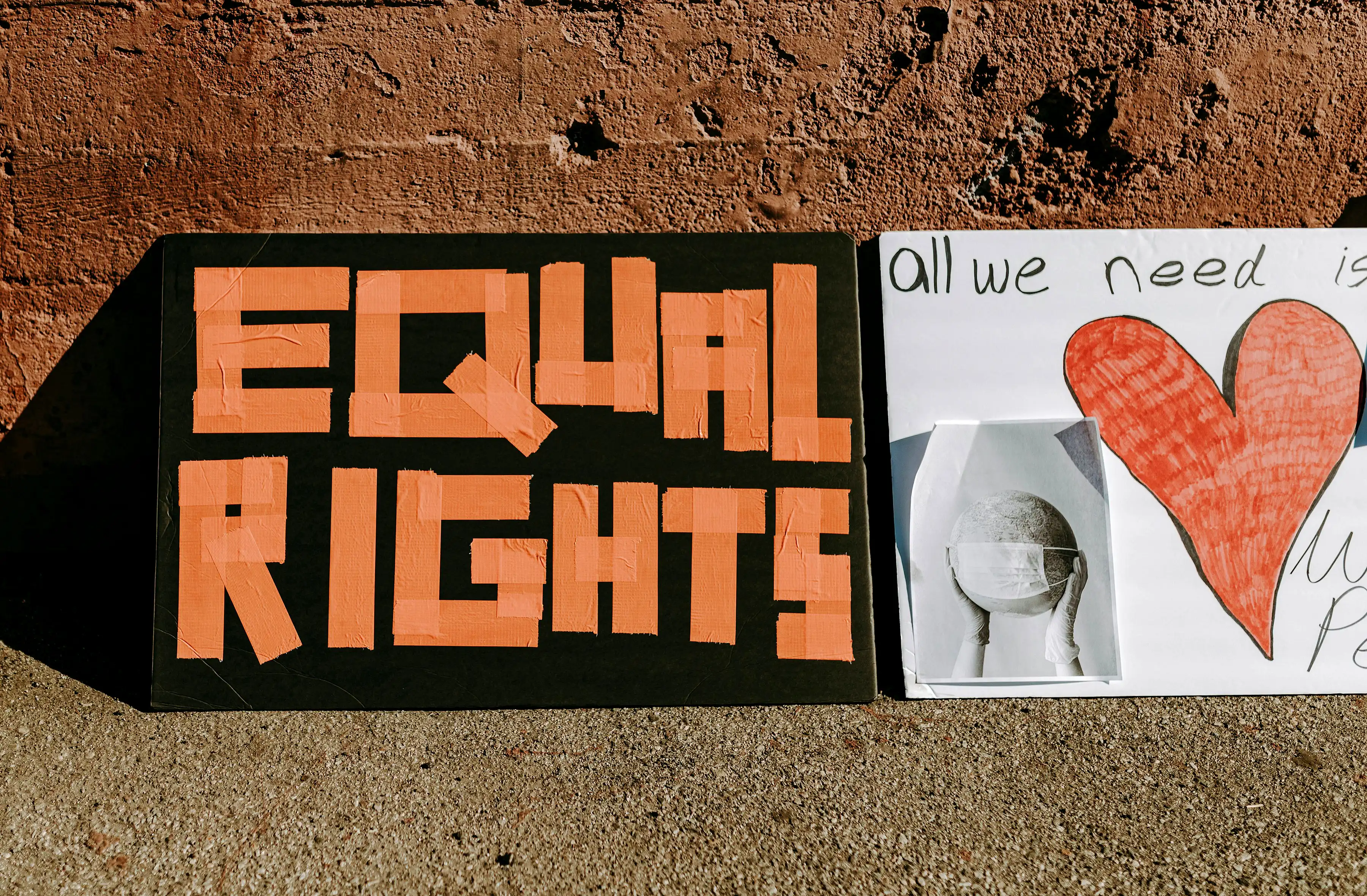 Picture of a banner on a brick wall with a graphic of a pair of hands holding a globe of the world, a hand drawn graphic of a red heart with the words ‘all we need is love’ and ‘Equal Rights’.