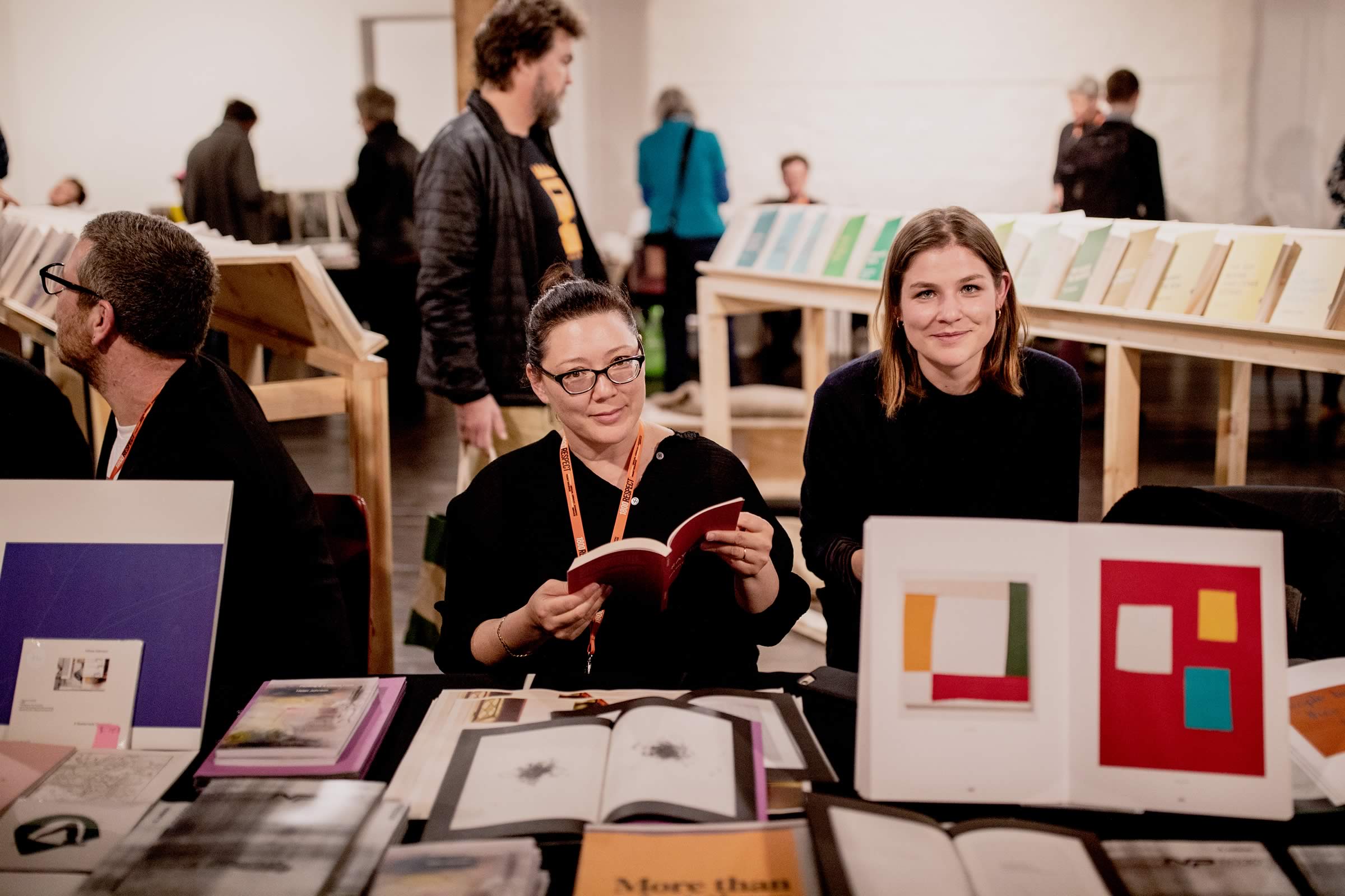 Photo of two smiling women stallholders seated behind a display of books. Photo: Rosie Hastie for The People’s Library 2018.