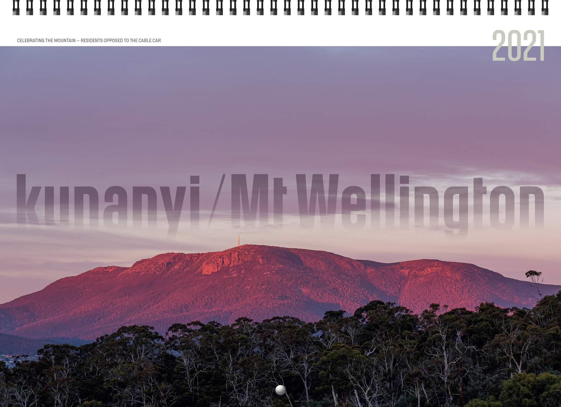 Image of the cover of the 2021 kunanyi / Mount Wellington calendar featuring a photo of kunanyi glowing purplish in the dawn light, with eucalypt forest in the foreground.