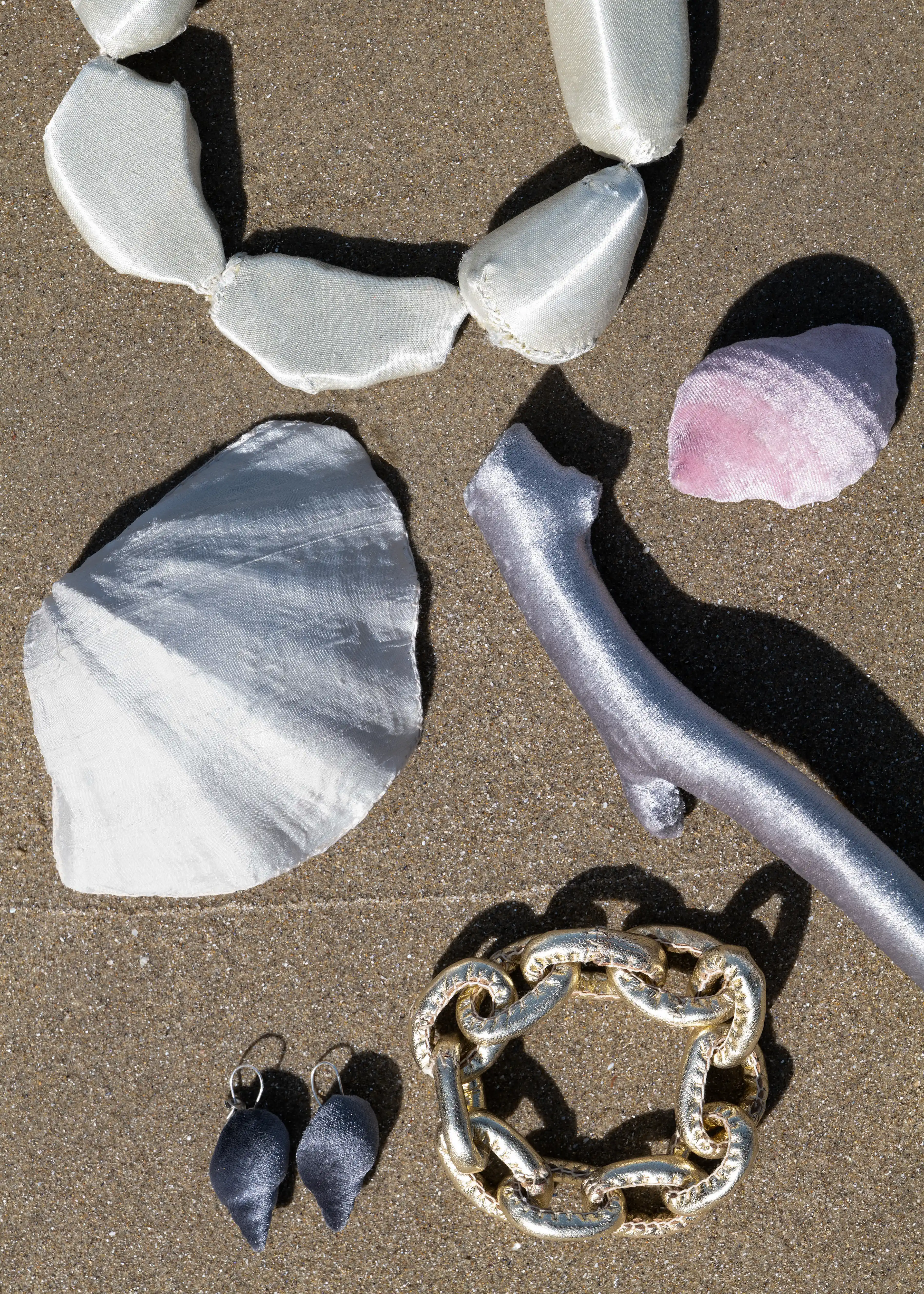 Image of a collection of six pieces of ocean-themed jewellery by Gabbee Stolp photographed against a background of sand.