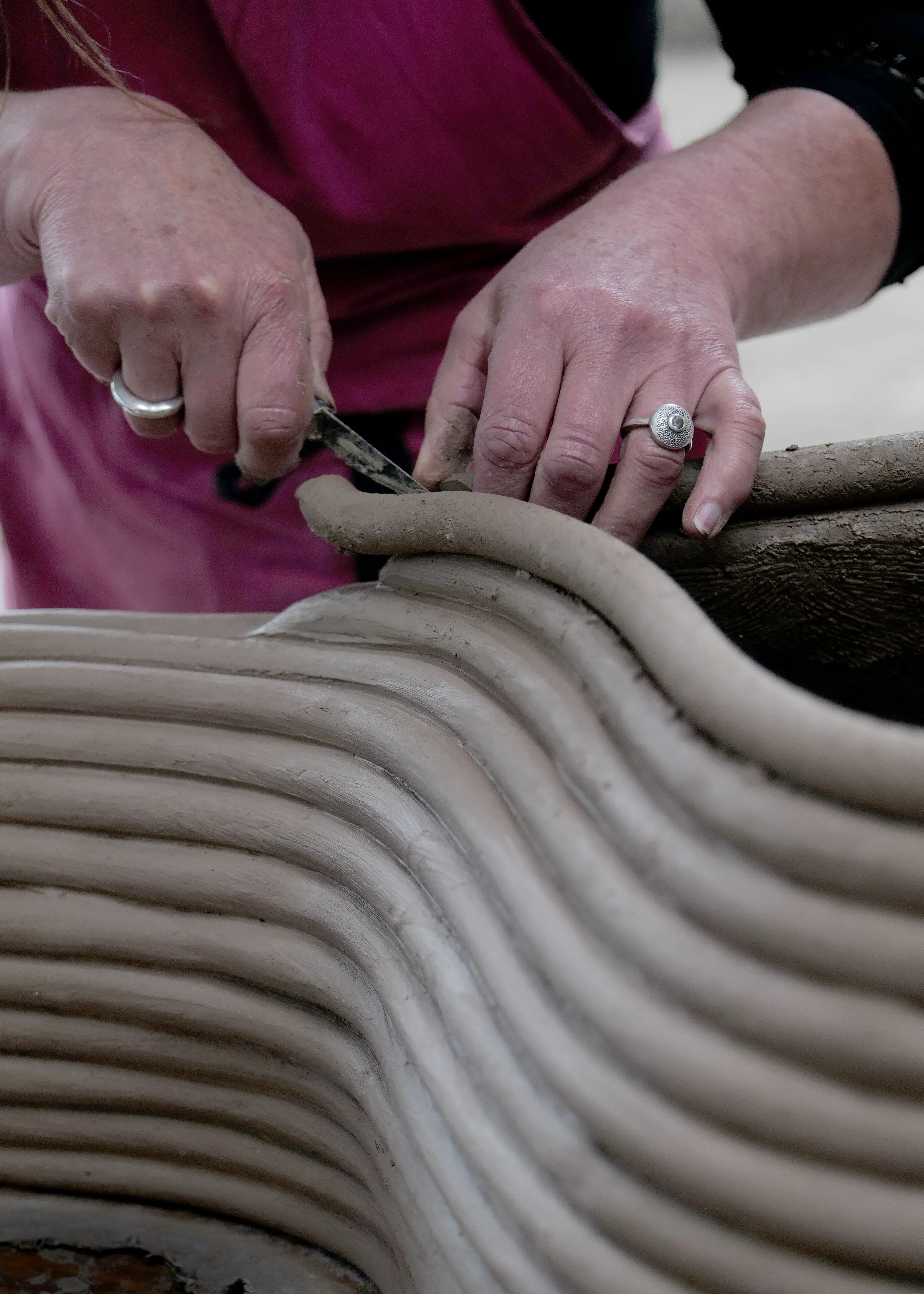 Image of a woman’s hands building layers of linear sausage-shaped clay to create an artificial home for the endangered Tasmanian handfish.