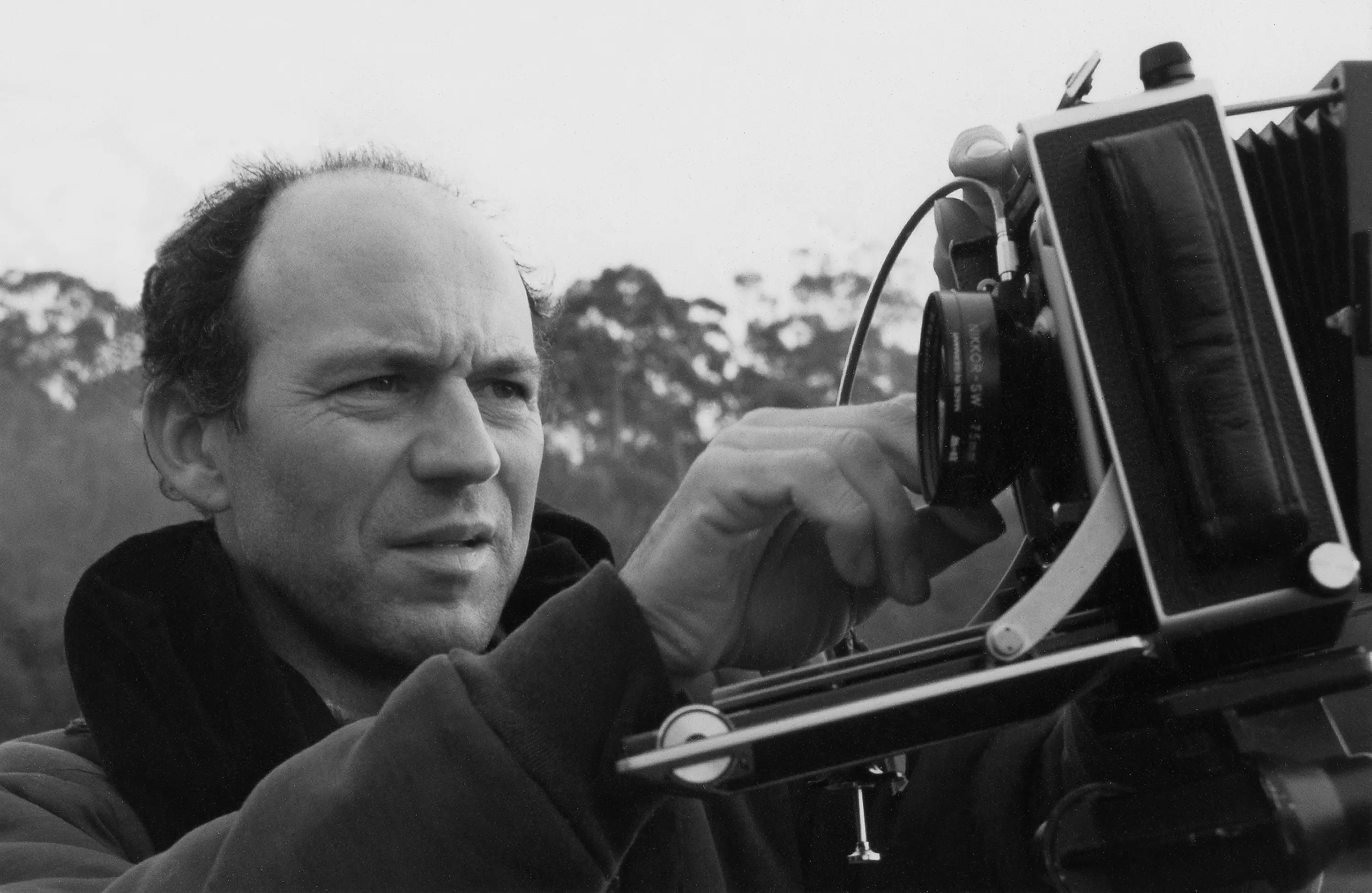 A black and white portrait photograph of Chris Bell with his large format Linhof Technikardan 4x5 camera.