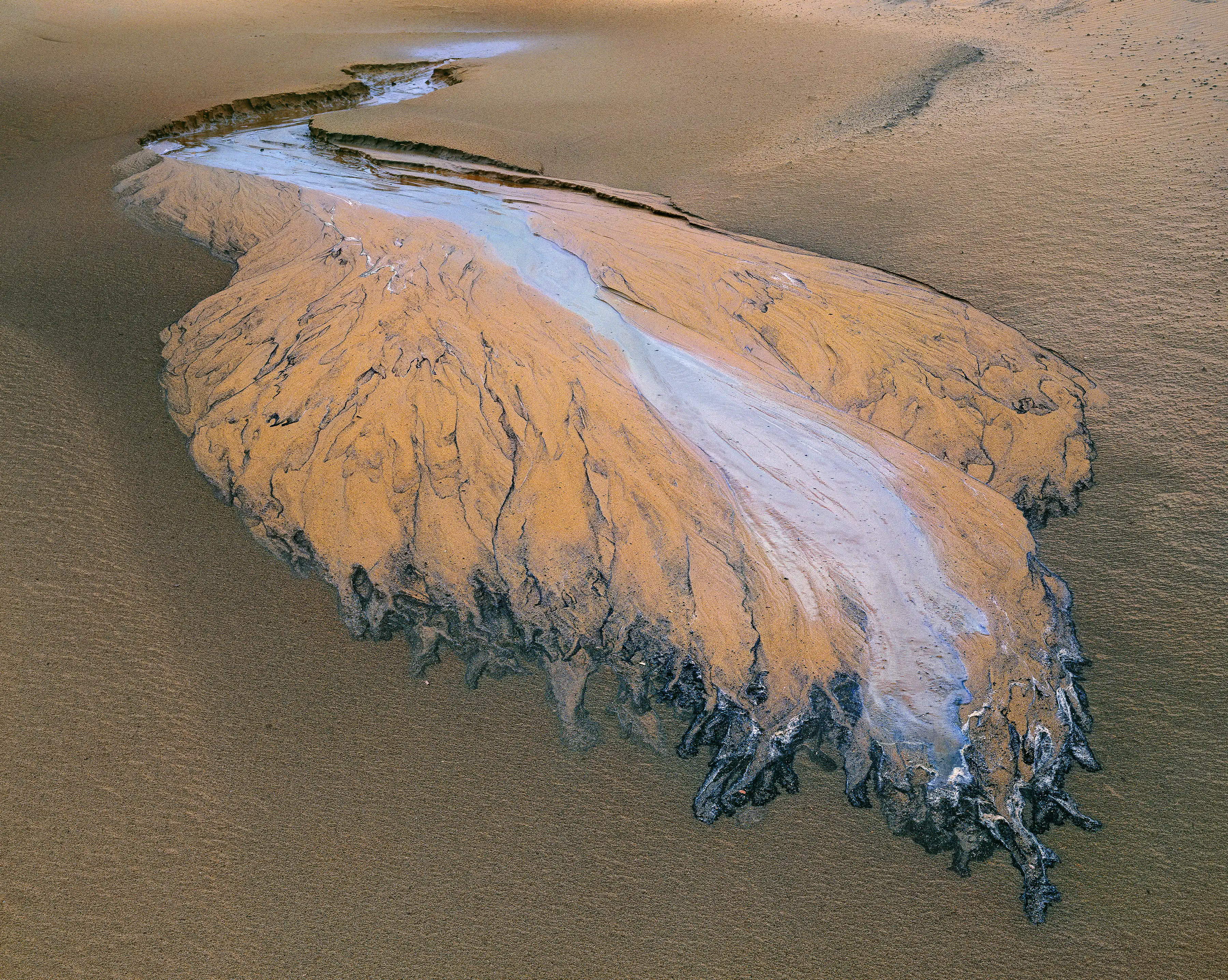 A close up image of a sand beach with an underground stream terminus creating highly patterned impressions in the sand.