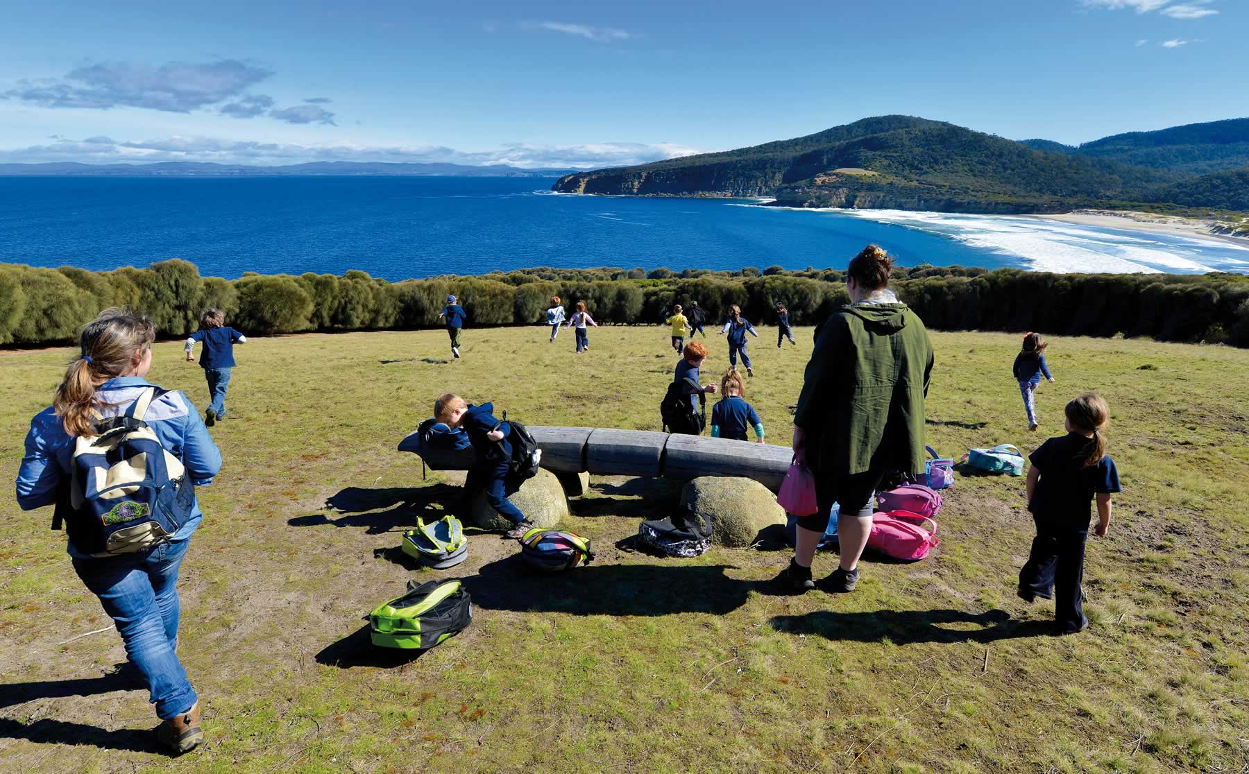 Photo of a large group of children playing in a clearing surrounded by sheoak scrub with the sea and beach and headland in the background. Photo courtesy of Peter Adams.