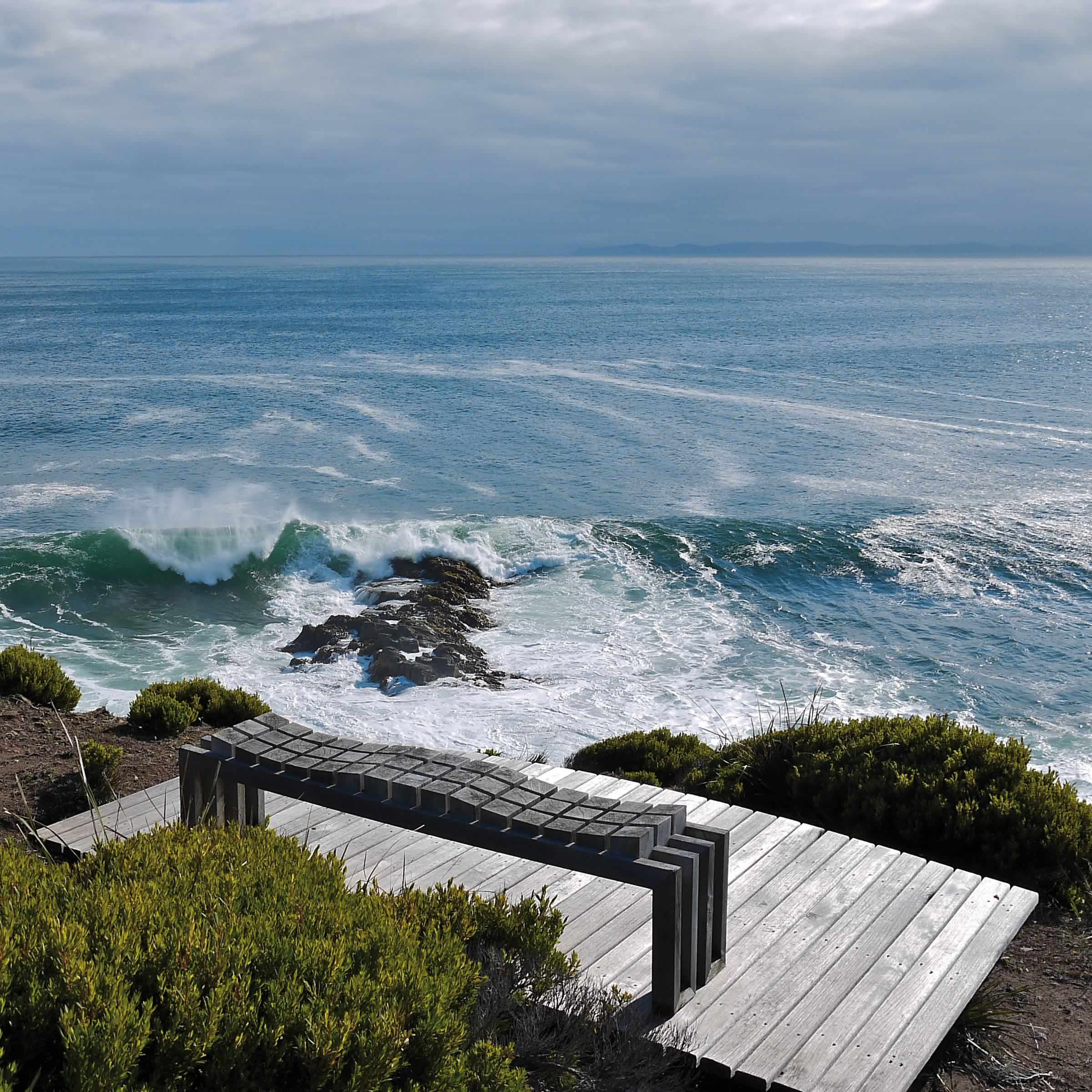 Photo of a rough sea with a black undulating bench seat on a timber platform in the foreground. Photo courtesy of Peter Adams.
