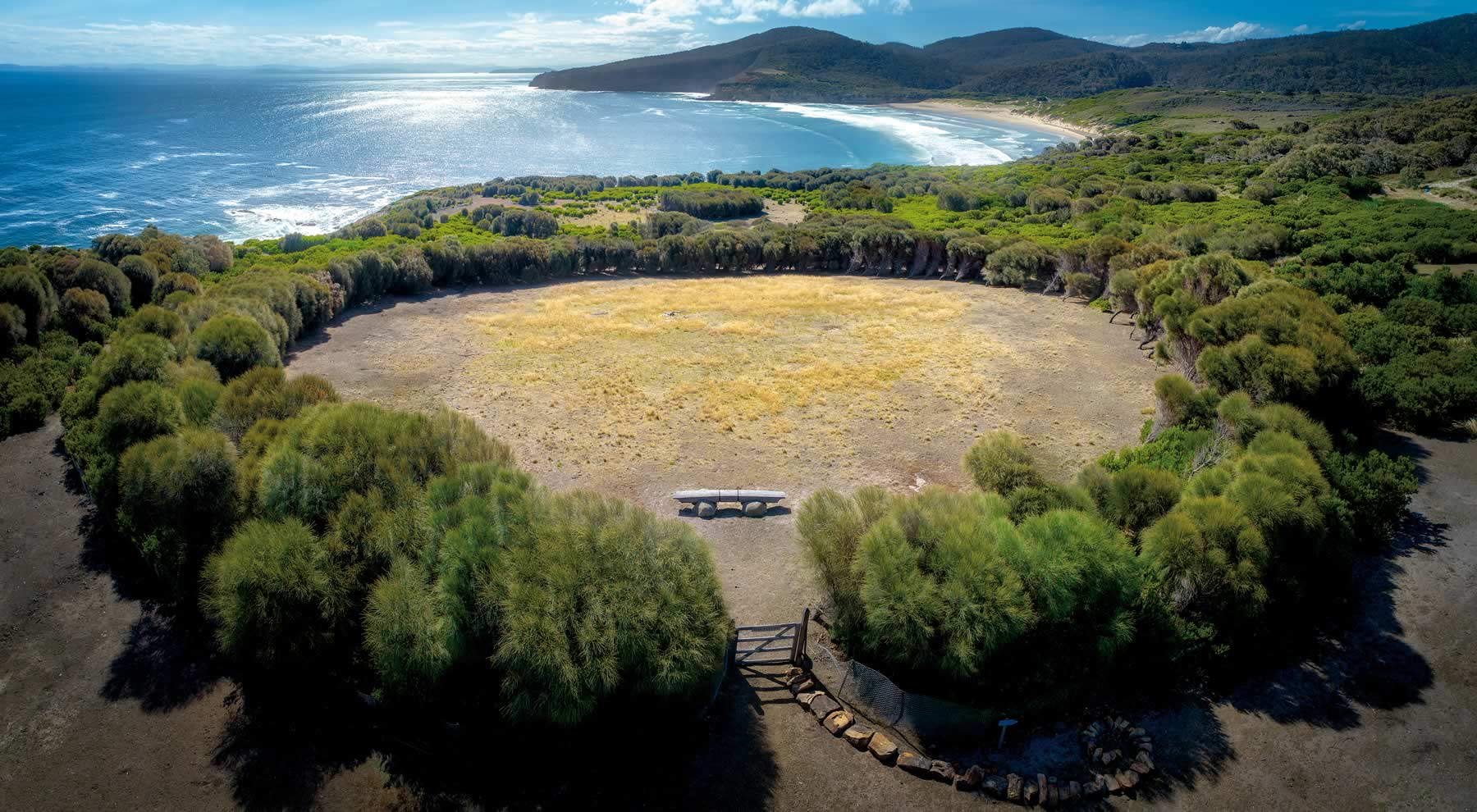 Photo from the air of a circular clearing surrounded by sheoak scrub with a bench in the circle and sea and beach and headland in the background. Photo courtesy of Peter Adams.