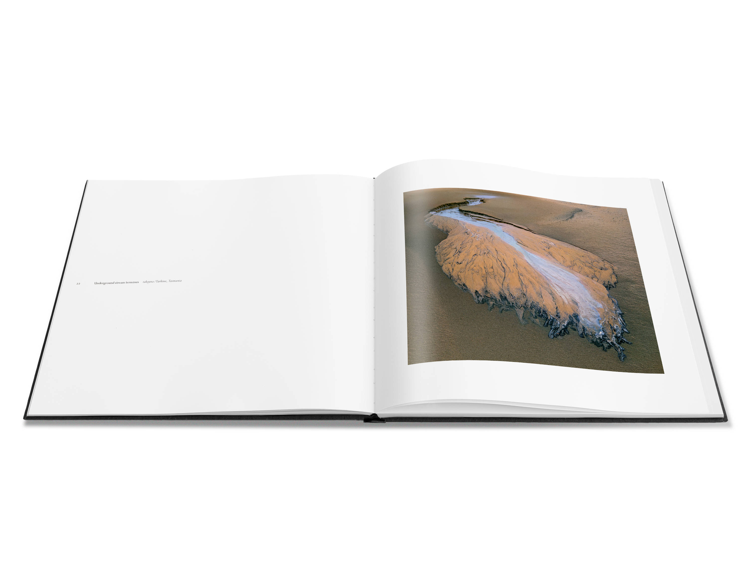 Image of a double page spread from the book featuring a close up image of a sand beach with an underground stream terminus creating highly patterned impressions in the sand.