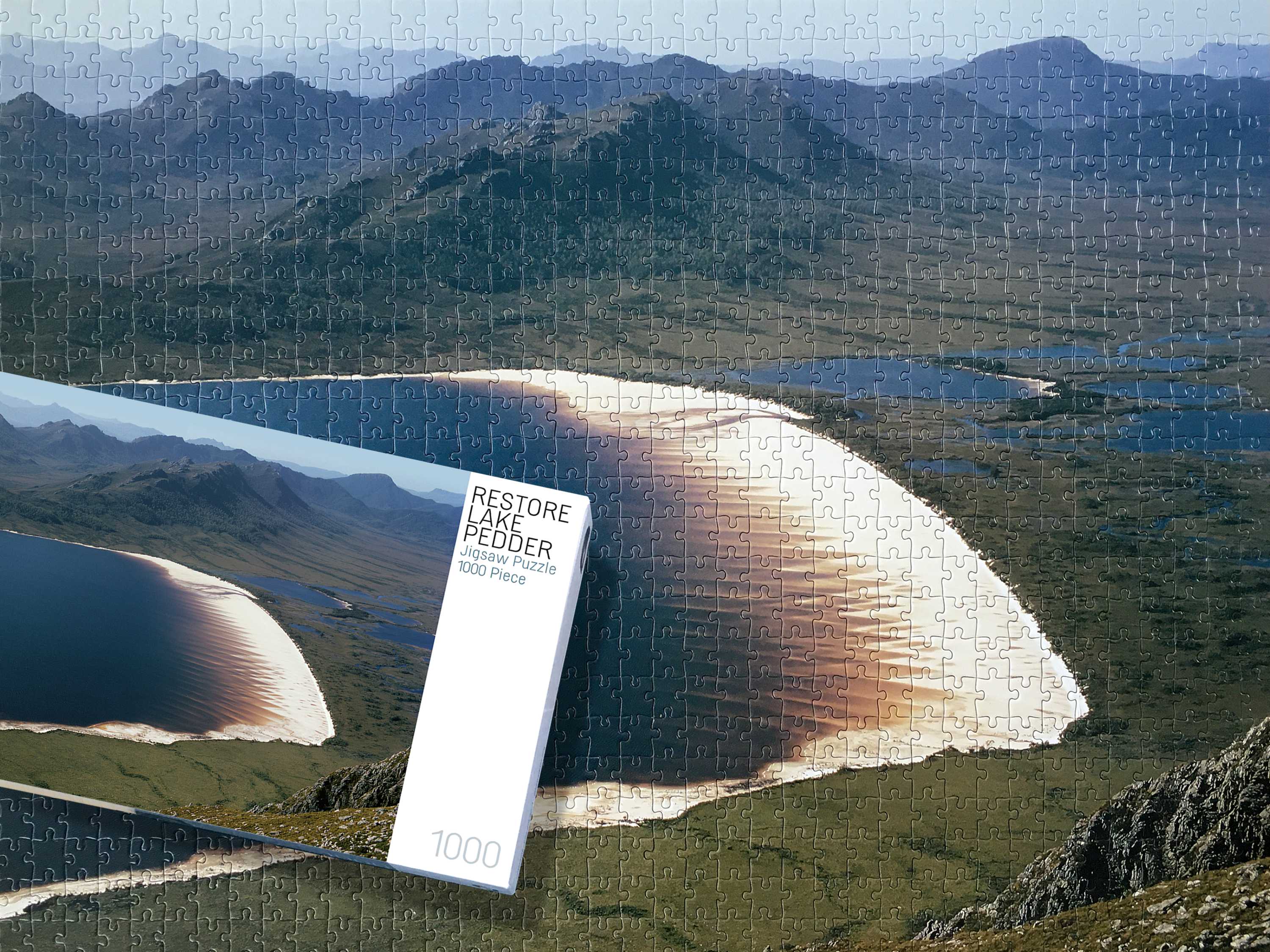 A montage with a background image of a completed Lake Pedder jigsaw and a boxed jigsaw sitting on top of the completed puzzle.